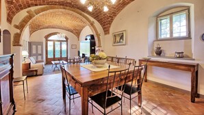 Un comedor espacioso con una gran mesa de madera, techo de ladrillo abovedado y vistas al exterior.