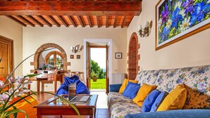 Un accogliente soggiorno con soffitto in legno, un divano floreale e vista su un giardino attraverso una porta aperta.