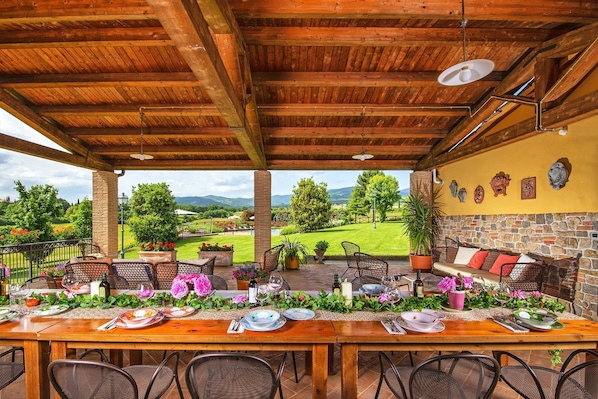 An outdoor dining area with a wooden table set for a meal, surrounded by chairs, with a view of a green landscape and mountains in the background. - Podere Sant'Angelo - Villa with private pool (Bibbiena)