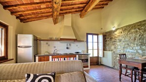 Une cuisine chaleureuse avec un plafond en bois, un mur en pierre et un coin repas comprenant une table et des chaises.