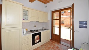 Une cuisine avec des meubles de couleur claire, une cuisinière à gaz et un évier. Une porte donne sur une cour intérieure, où l’on peut apercevoir un bâtiment en briques à l’extérieur.
