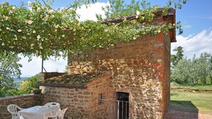 A stone building with a brick roof, a small door, and a table with chairs outside.