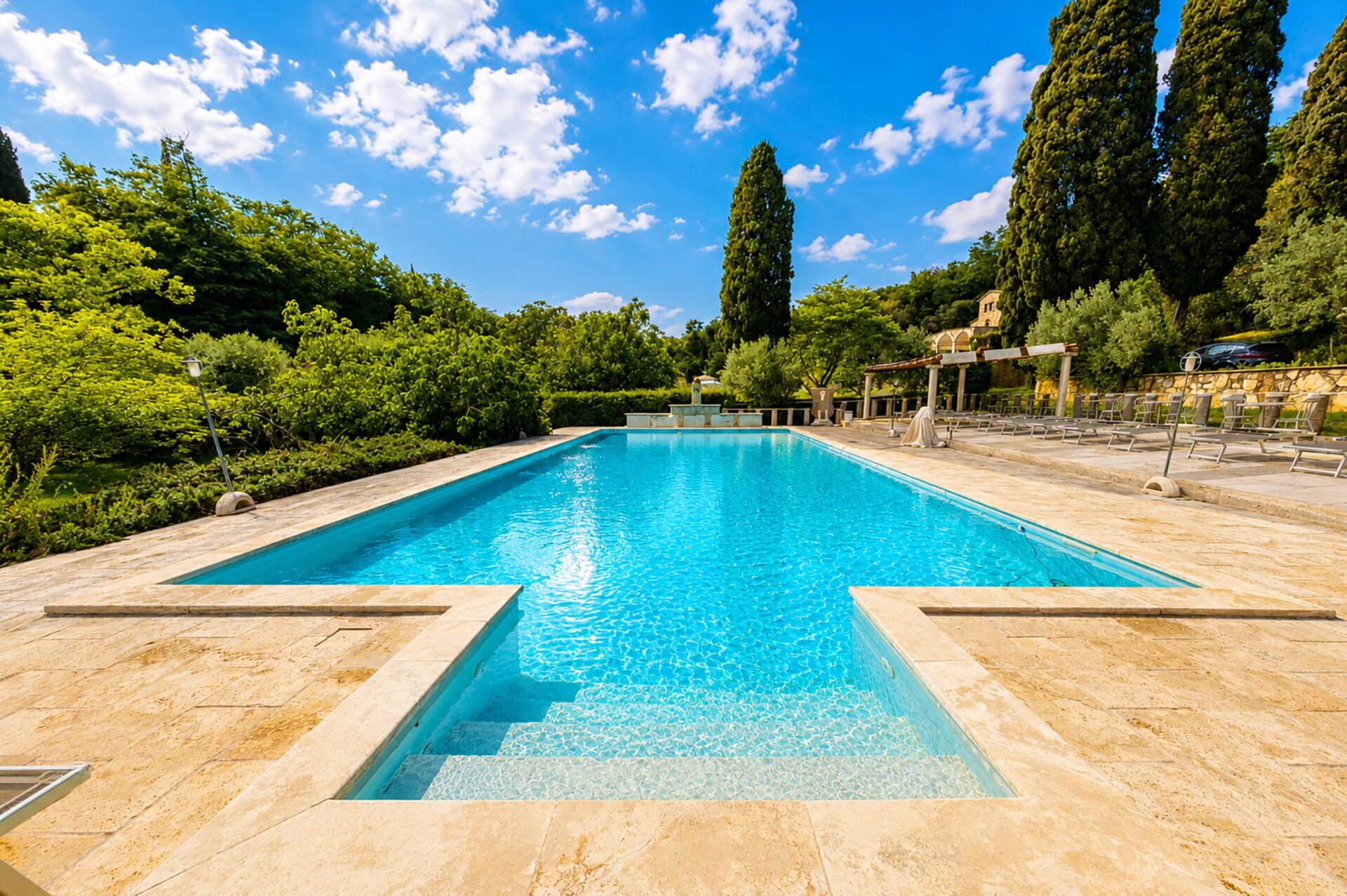 Ein rechteckiger Pool mit klarem, blauen Wasser, umgeben von einer gefliesten Terrasse.