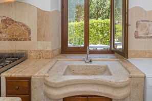 Una cocina con un lavamanos de piedra, una estufa a gas y una ventana con vistas al verdor.