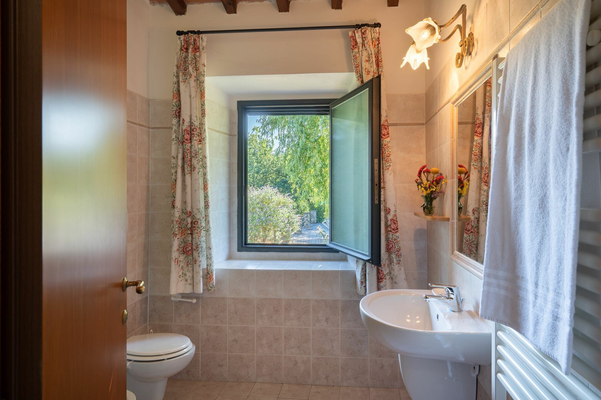A bathroom with a toilet, sink, and a window with a view of greenery.