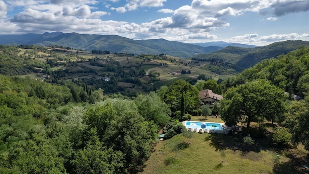 Ein Poolbereich mit Liegestühlen und einem kleinen Haus in einer üppigen, hügeligen Landschaft.
