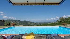 A swimming pool with lounge chairs and a view of the countryside.