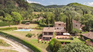 A stone house with a pool, surrounded by lush greenery and hills.