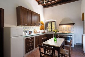 A kitchen with wooden cabinets, a white refrigerator, a dining table with chairs, and a window with a view.