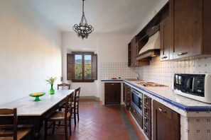 A kitchen with a dining table, chairs, a hanging light fixture, cabinets, a microwave, and a window with a view.