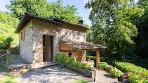 Une petite maison en pierre avec un toit de tuiles, une porte en bois et un petit porche agrémenté de plantes en pot.