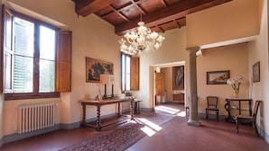 Una habitación amplia con alto techo de madera, un candelabro y ventanas grandes con contraventanas.