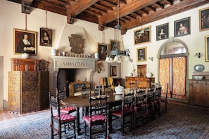 Una sala da pranzo tradizionale con un grande tavolo in legno, sedie decorate e un camino.