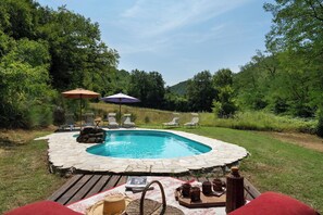 A swimming pool with lounge chairs and umbrellas, surrounded by greenery.