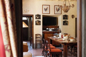 Comedor con mesa de madera dispuesta para una comida, sillas, una araña y cuadros en la pared.