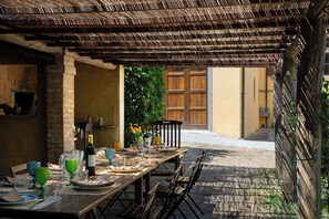 An outdoor dining area with a rustic wooden table set for a meal, surrounded by chairs.