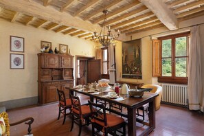 A dining room with a wooden table and chairs, a chandelier, and a window with a view of greenery.