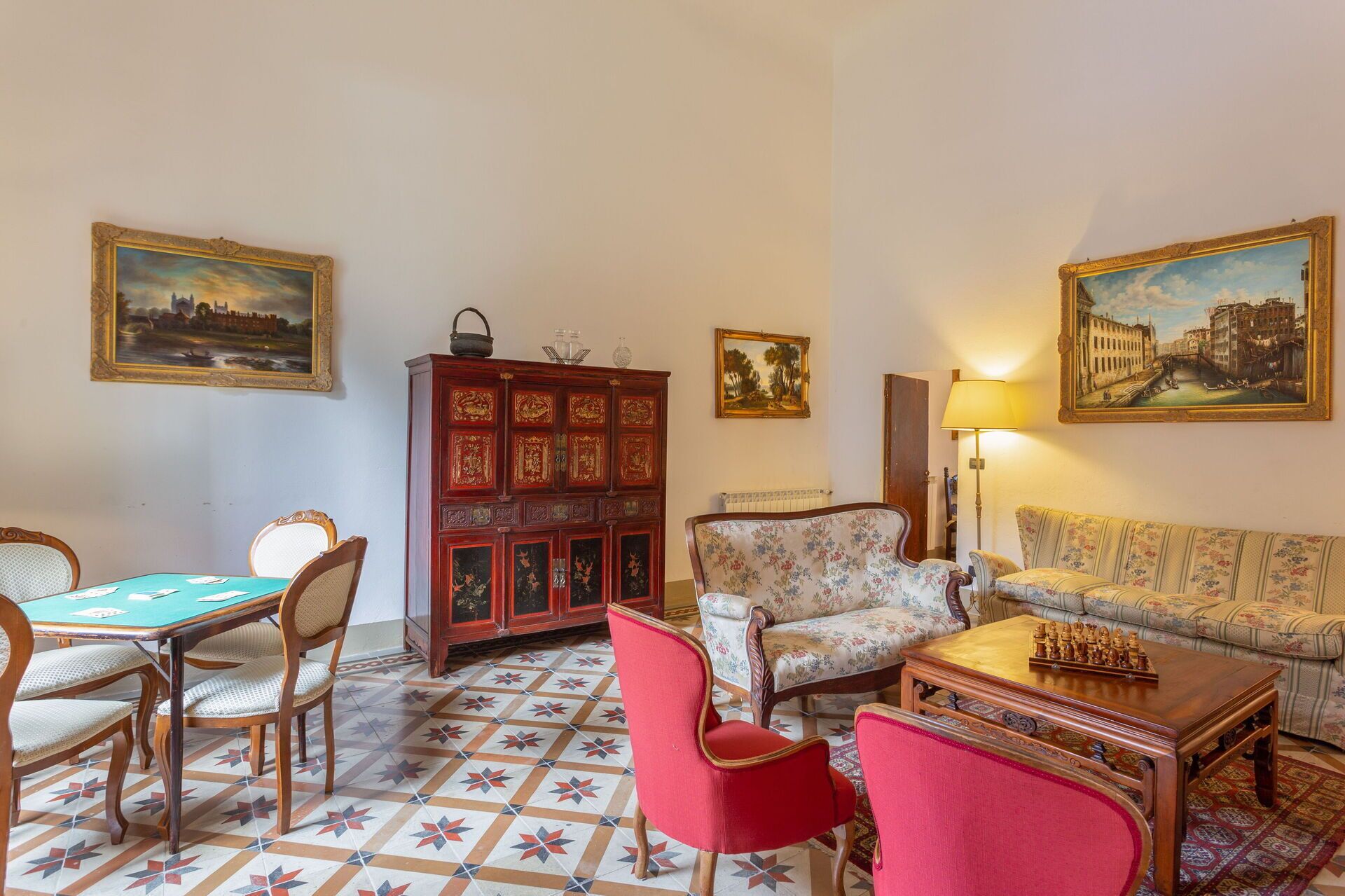 A room with a dining table, chairs, a sofa, a cabinet, and paintings on the walls.