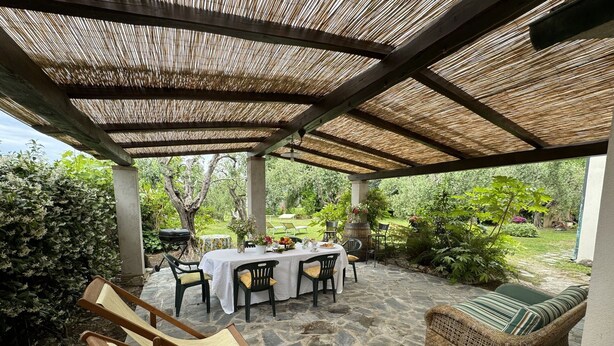 An outdoor patio with stone flooring, a covered seating area with chairs and a table, and a wicker sofa.