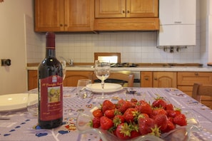A kitchen with wooden cabinets, a white tiled backsplash, a wine bottle, a glass, and a table with strawberries. - Nice apartment for 4 guests with private pool, WIFI, TV and pets allowed (Castiglion Fiorentino)