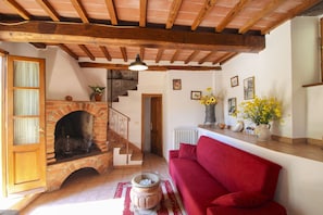 A cozy living room with a red sofa, a fireplace, and a staircase leading to an upper level. - Nice apartment for 4 guests with private pool, WIFI, TV and pets allowed (Castiglion Fiorentino)
