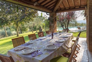 Un espace de restauration en plein air avec une table dressée pour quatre personnes, entourée de chaises, sous une pergola en bois.