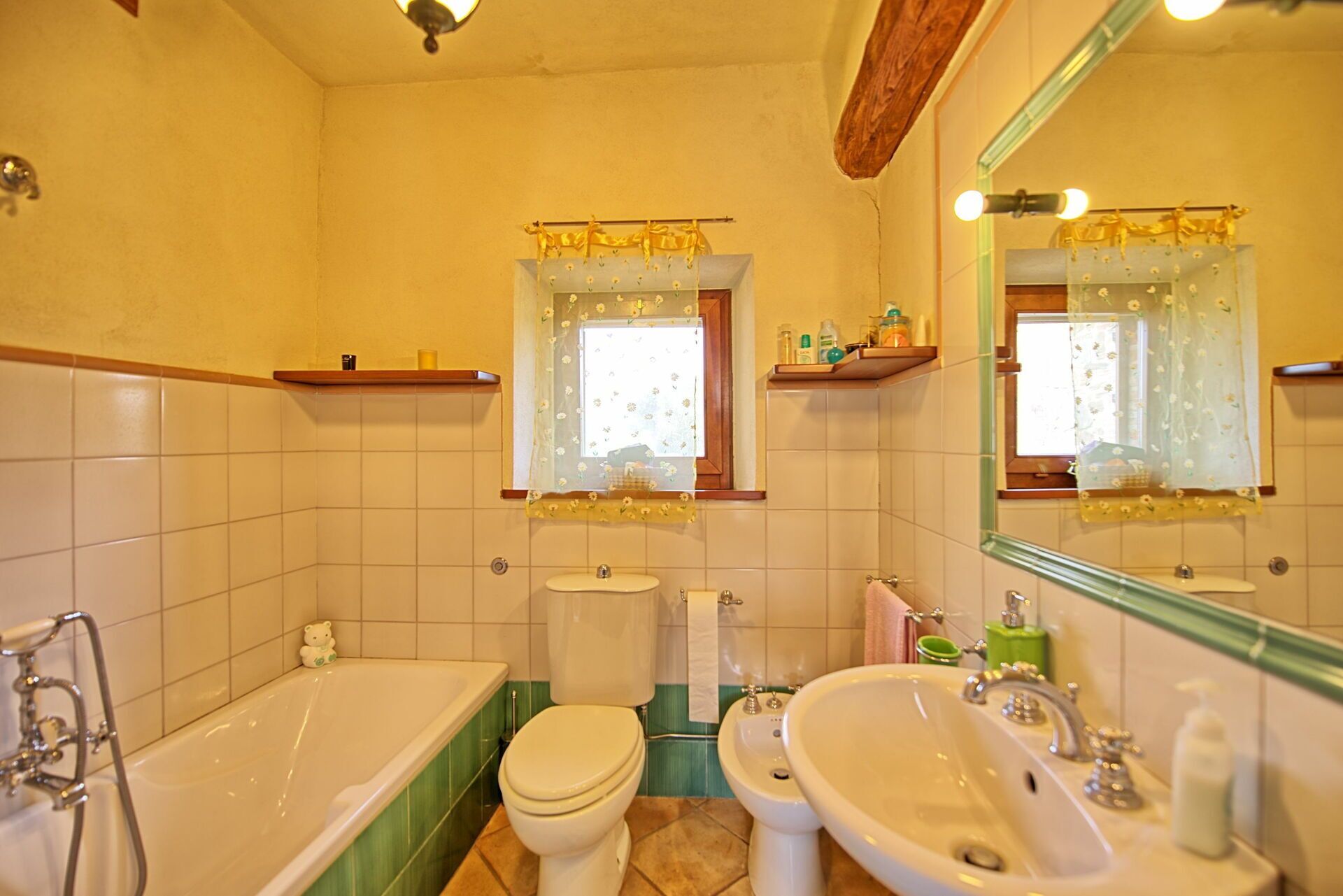 Un baño con bañera, inodoro, bidé y lavabo. Hay repisas sobre el inodoro y el lavabo, y un espejo sobre el lavabo.