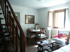 A dining area with a wooden table and chairs, a painting on the wall, and a window with curtains.