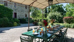 An outdoor dining area with a table set for breakfast, surrounded by greenery and a stone building.