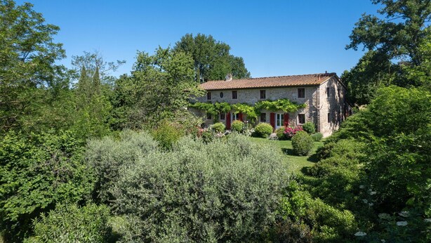 A stone house with a tiled roof, surrounded by lush greenery and trees.