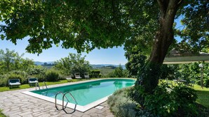 A swimming pool with stone tiles, surrounded by greenery and a view of distant hills.