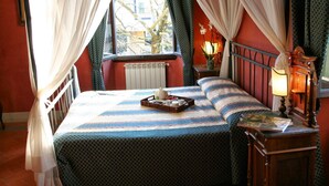 Uma cama com uma bandeja de itens de café da manhã, uma luminária de cabeceira e vista para o exterior através de uma janela com cortinas.