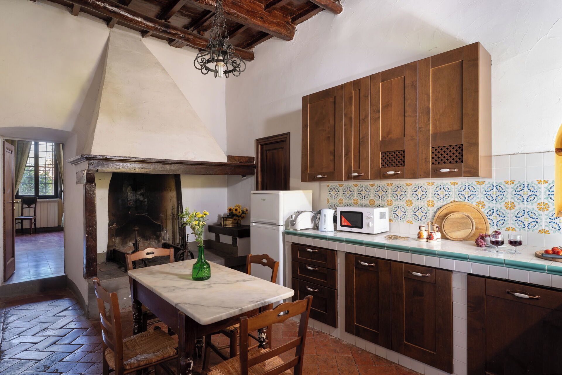 A kitchen with wooden cabinets, a marble countertop, a microwave, and a tiled backsplash.