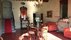 Uma área de refeições com mesa de madeira, cadeiras, um vaso com flores, um candelabro e uma escadaria com tapete vermelho.