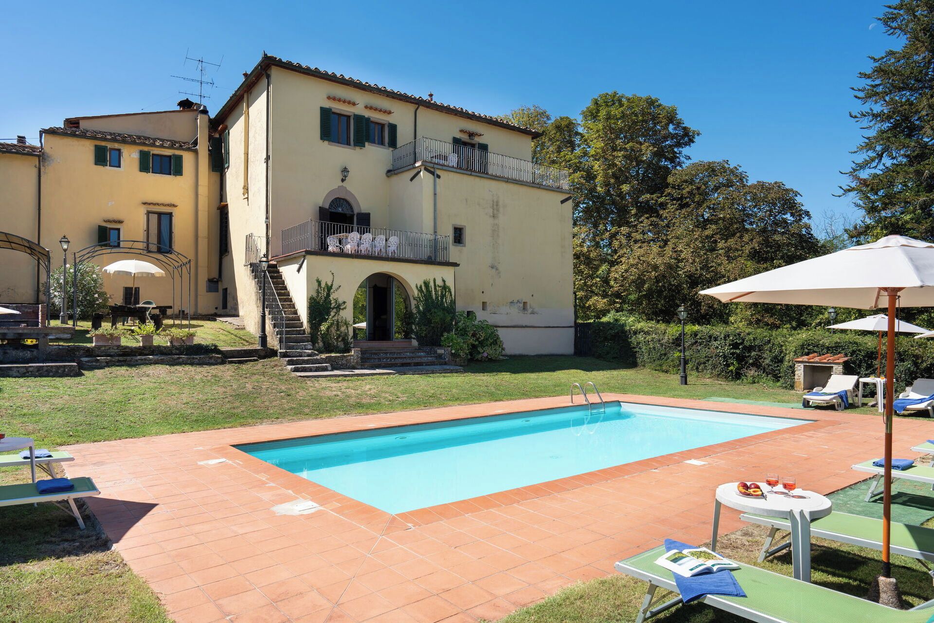 A swimming pool with a patio area, a covered seating area, and a building with a balcony.
