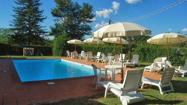 Piscina com cadeiras de praia e guarda-sóis, cercada por vegetação.