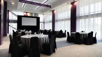 Een vergaderzaal met ronde tafels, stoelen, een groot scherm en een podium.