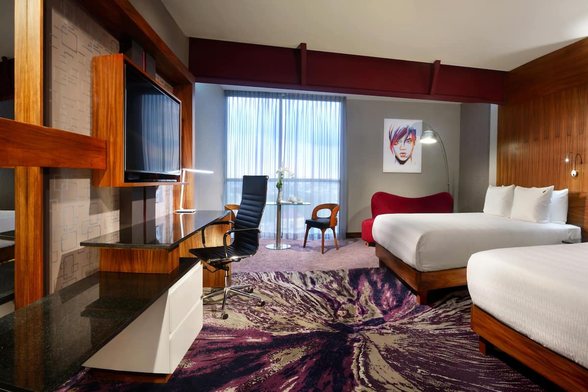 Ein Hotelzimmer mit Bett, Schreibtisch, Stuhl, Fernseher und einem großen Fenster.