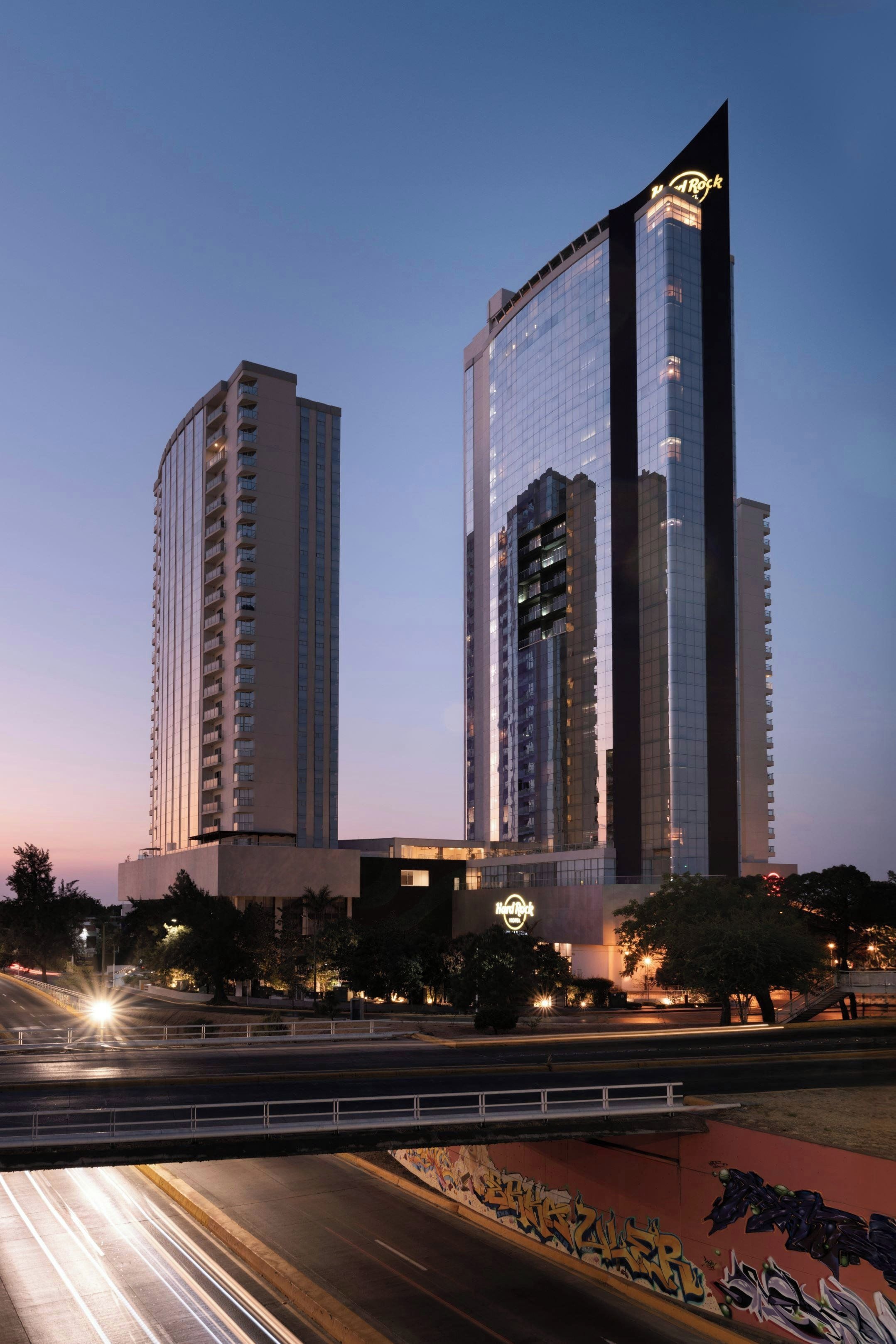 A modern hotel with a prominent glass facade and a distinctive logo on the top.