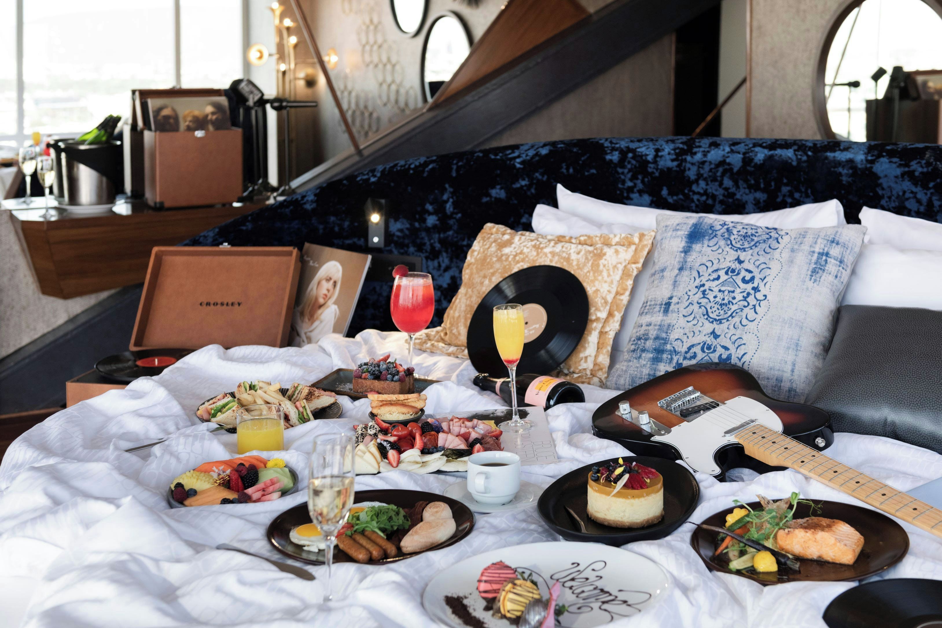 A bed with a variety of food items, drinks, and a guitar, suggesting a musical theme.