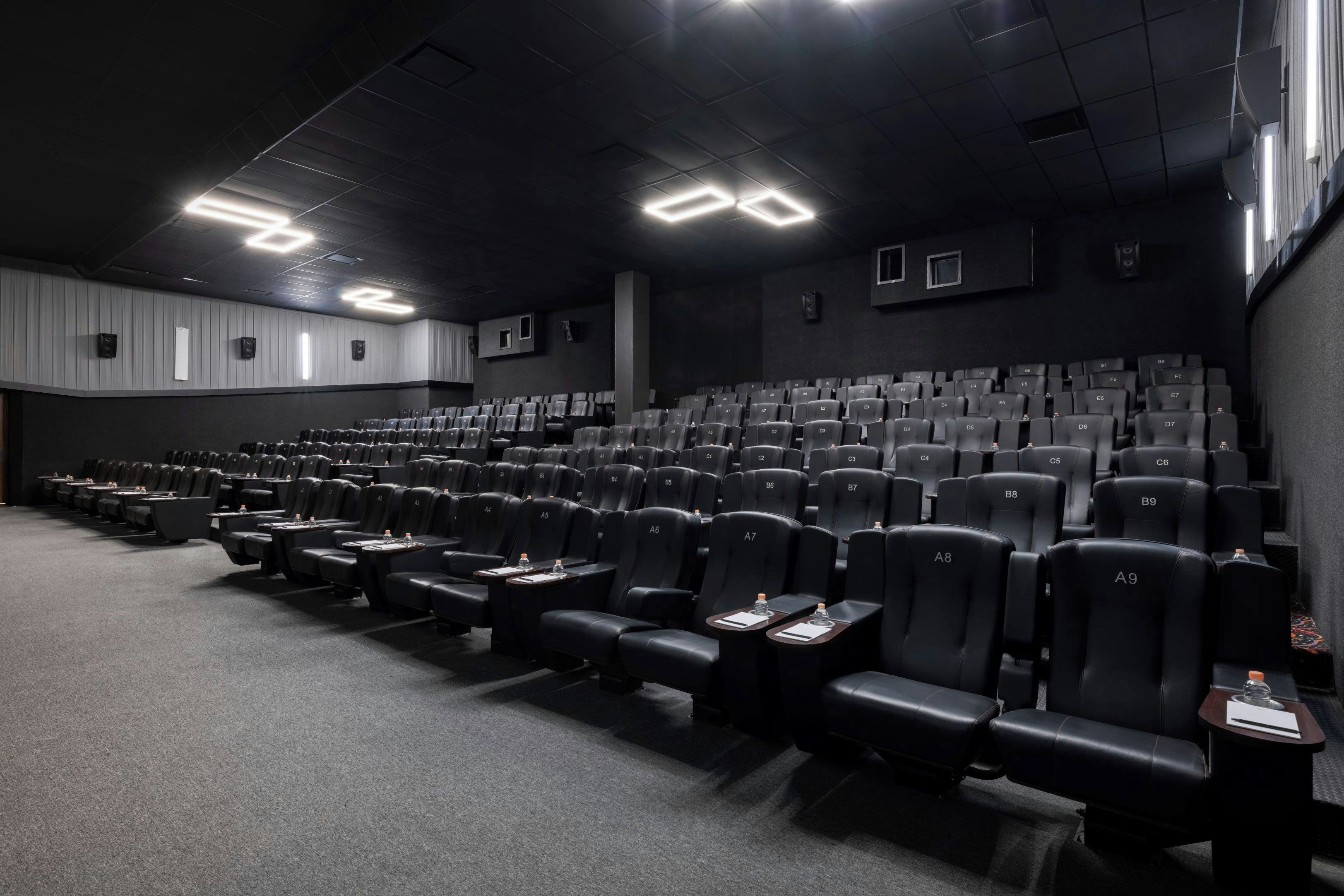 Una sala cinematografica con file di sedili in pelle nera, tavolini individuali con bottiglie d'acqua e illuminazione a soffitto.