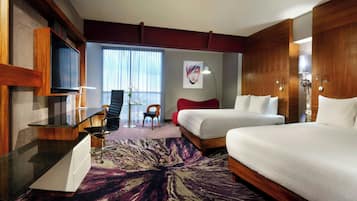 A hotel room with a bed, a desk with a chair, a television, and a large window with curtains.