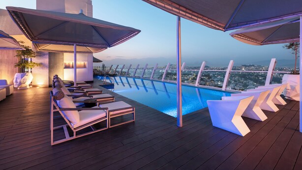 Un espace piscine aménagé sur le toit, avec des chaises longues et des parasols, offrant une vue sur le paysage urbain au crépuscule.