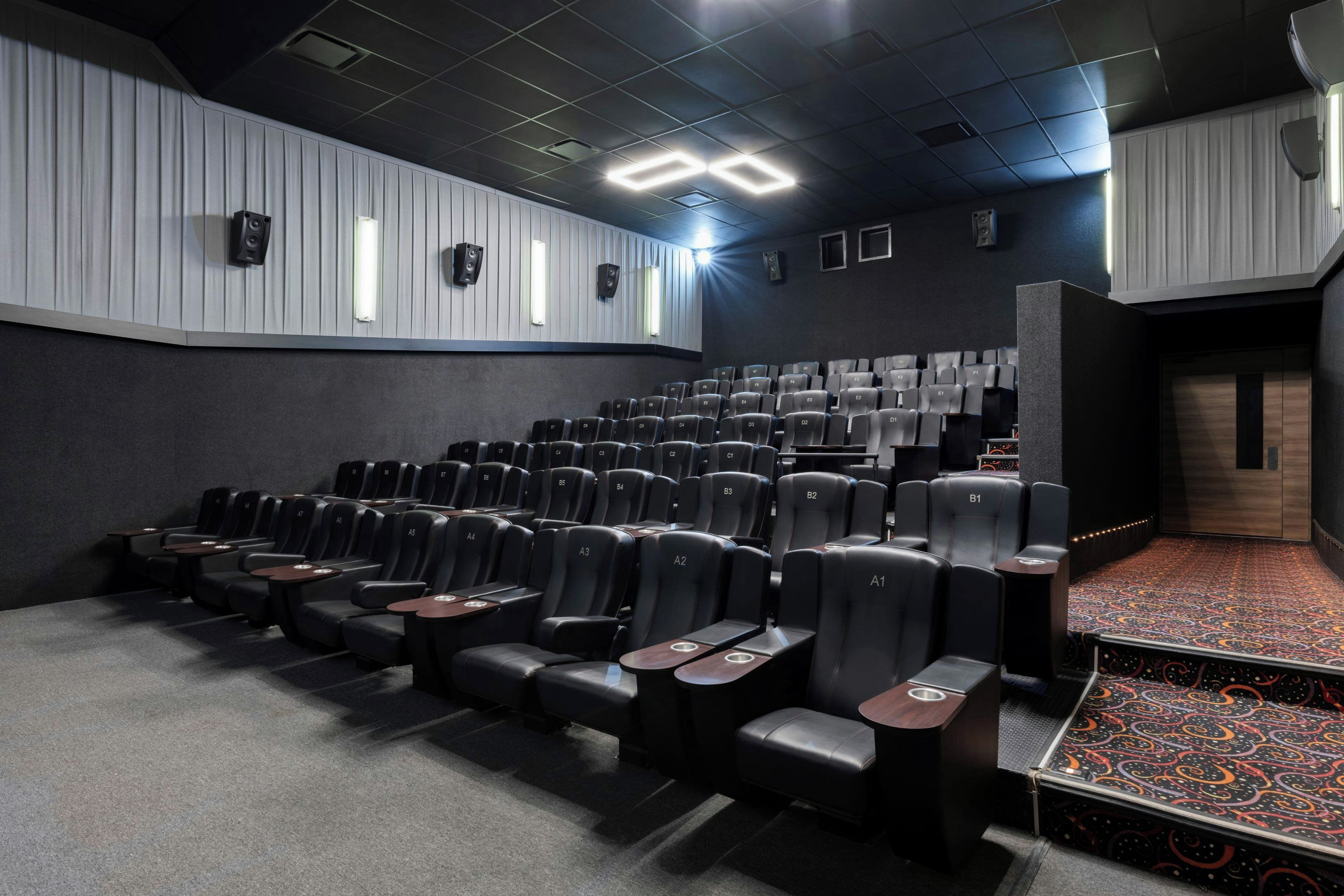 Un teatro con filas de asientos negros, una alfombra estampada y un escenario con un diseño colorido.