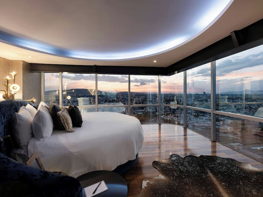 A modern bedroom with a large bed, a city view, and a unique ceiling design.
