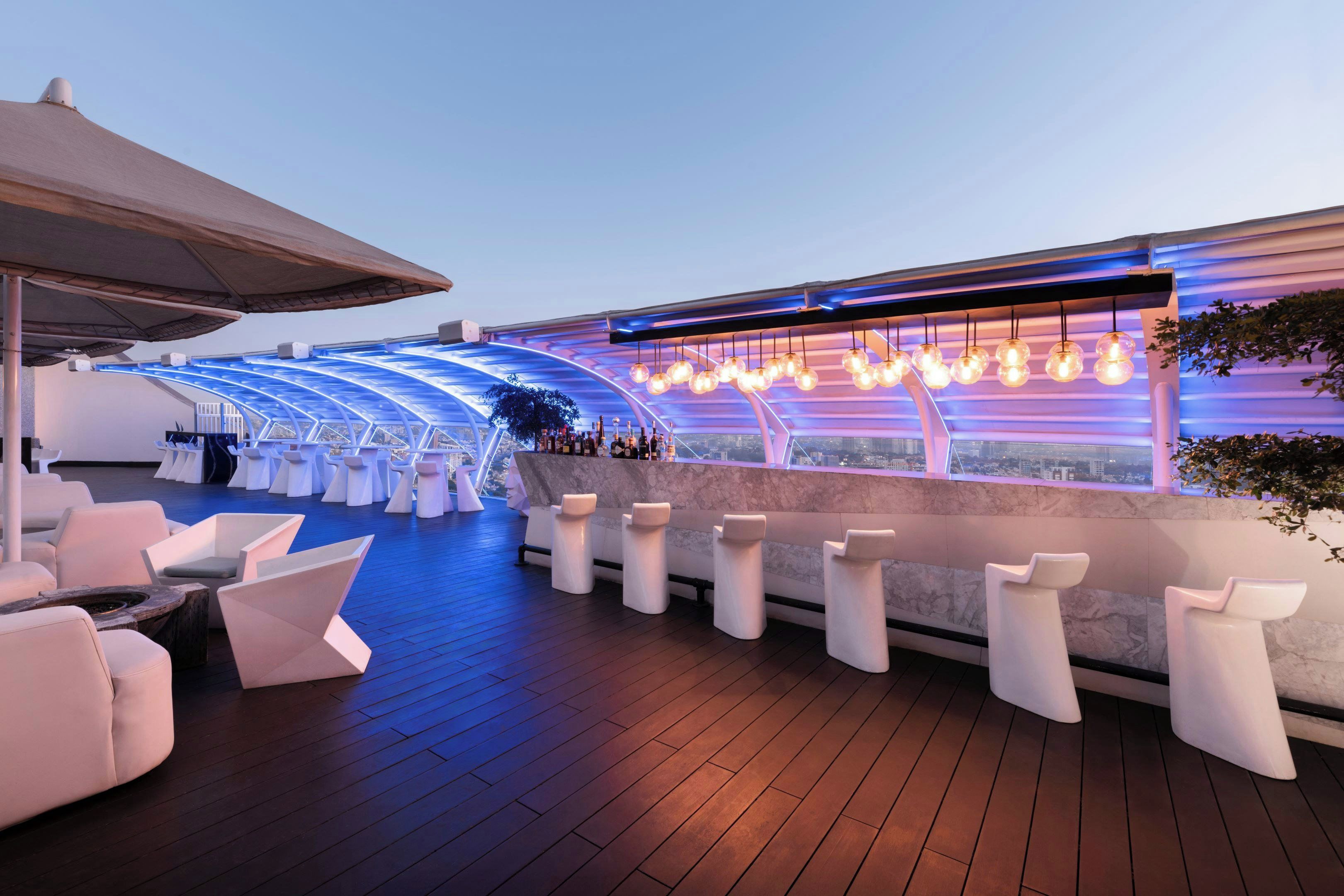 A rooftop bar with a curved ceiling, white bar stools, and a view of the cityscape.