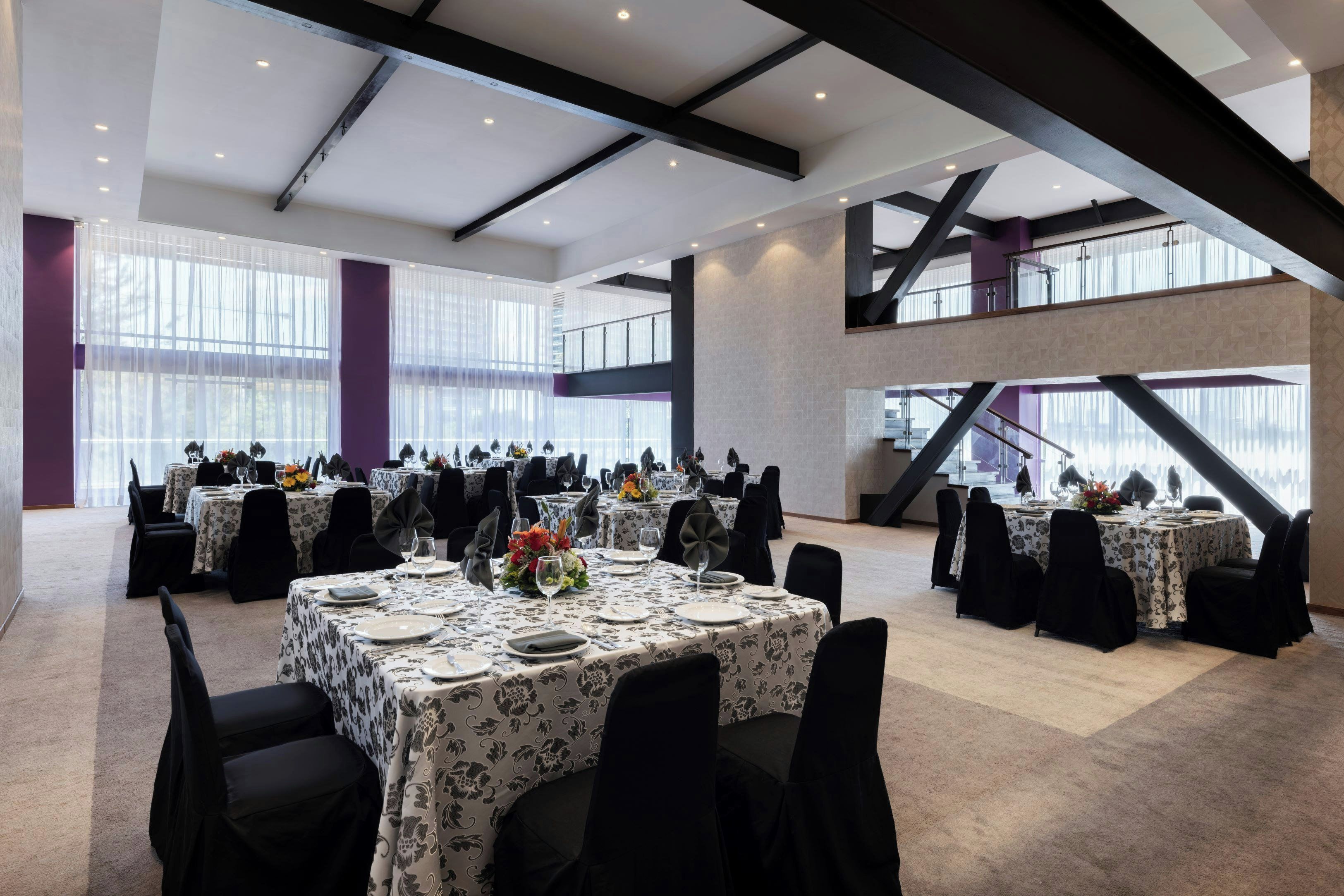 A spacious conference room with multiple tables set for dining, large windows, and a high ceiling with exposed beams.