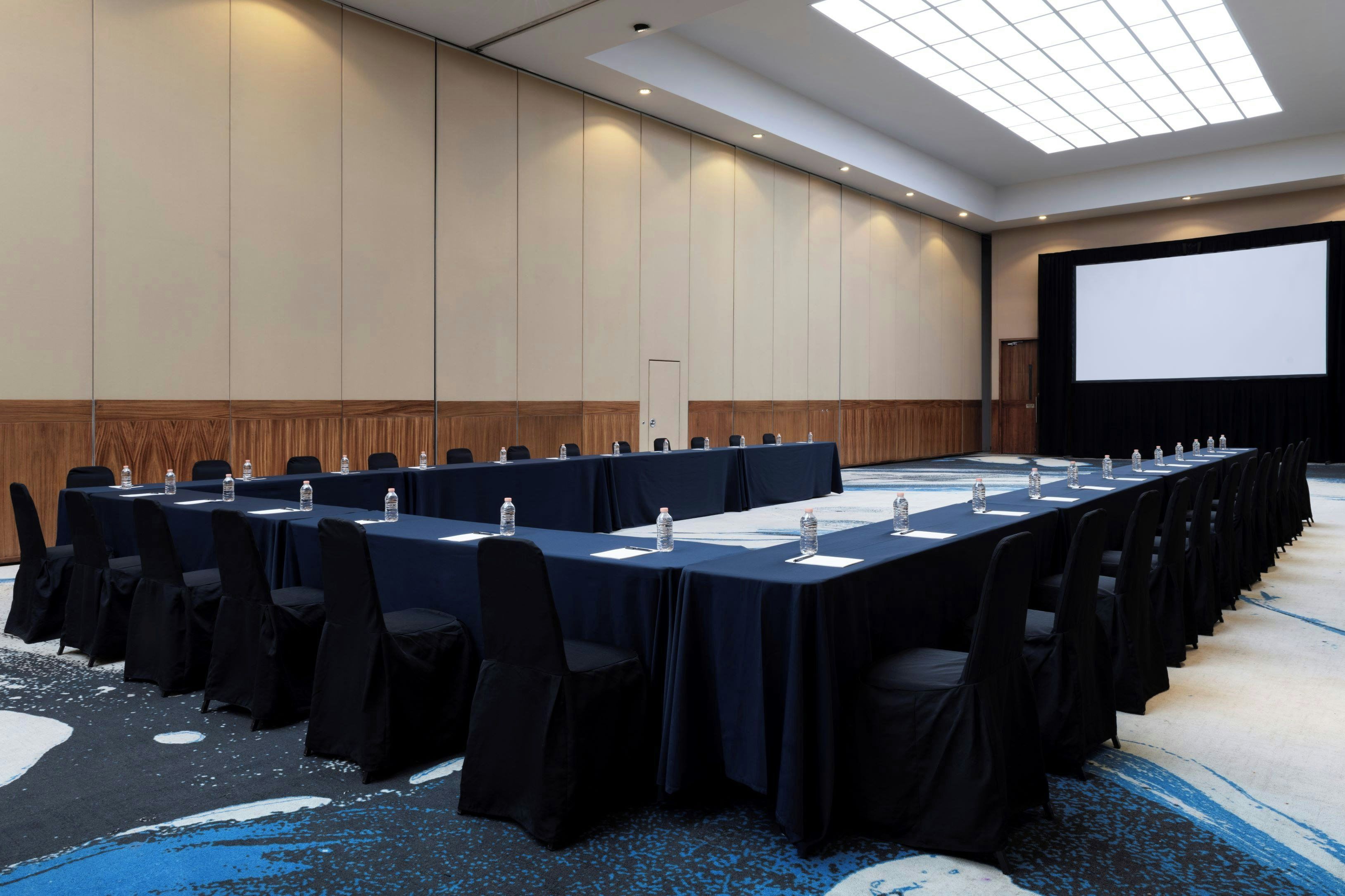 A conference room with a long table, chairs, and a projector screen.