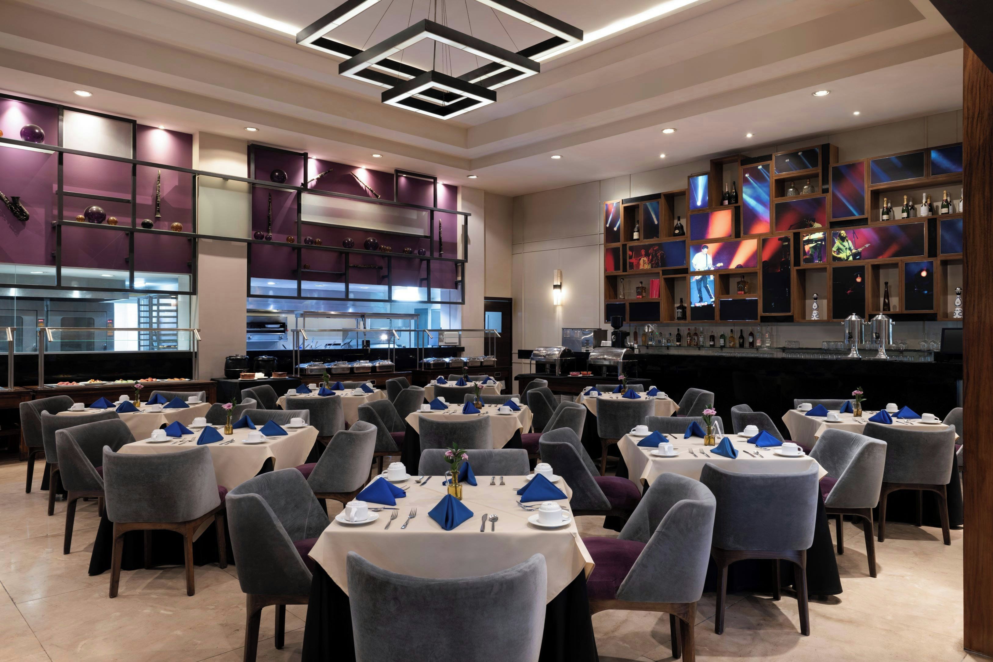Un restaurant avec plusieurs tables dressées pour le service, un bar bien garni de bouteilles variées et une cuisine située à l’arrière-plan.