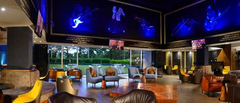 A modern lounge area with leather sofas, a coffee table, and a large TV screen displaying a band.